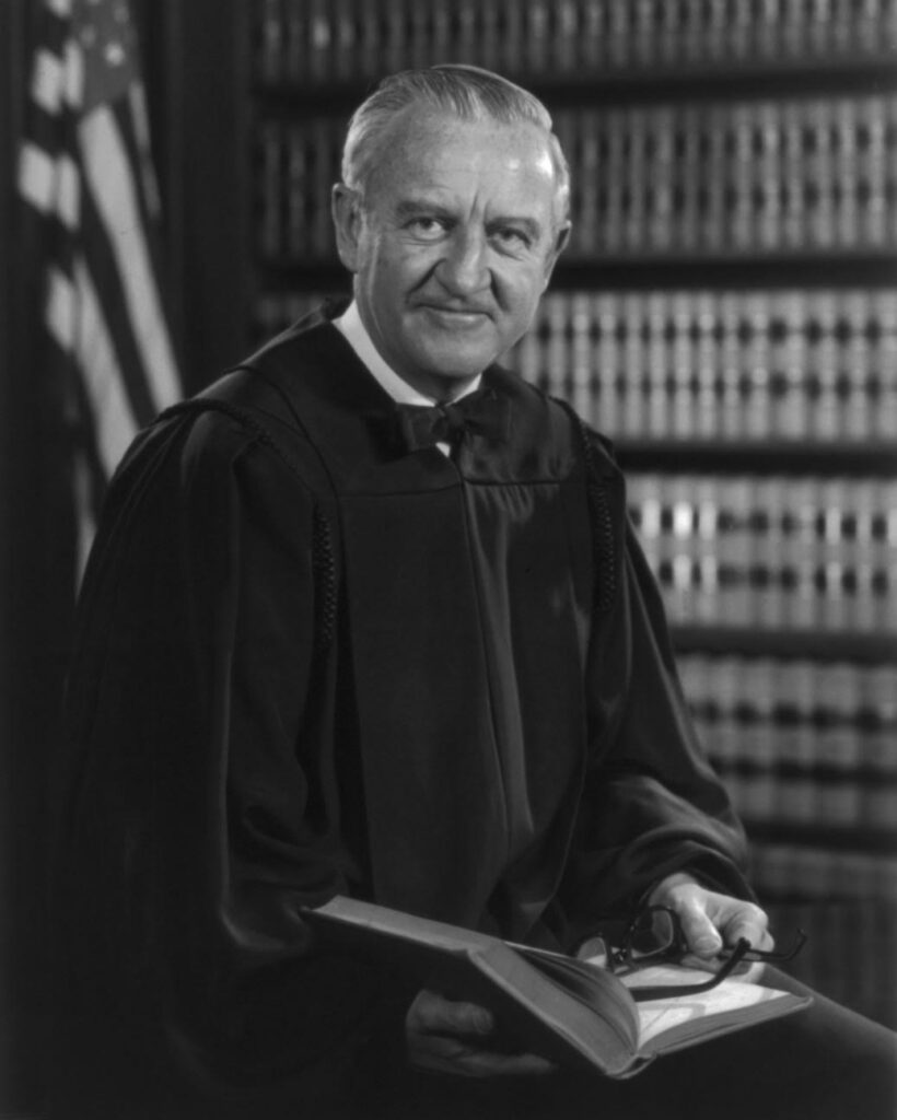 Justice Stevens Portrait in robes in front of a law library and a U.S. flag.