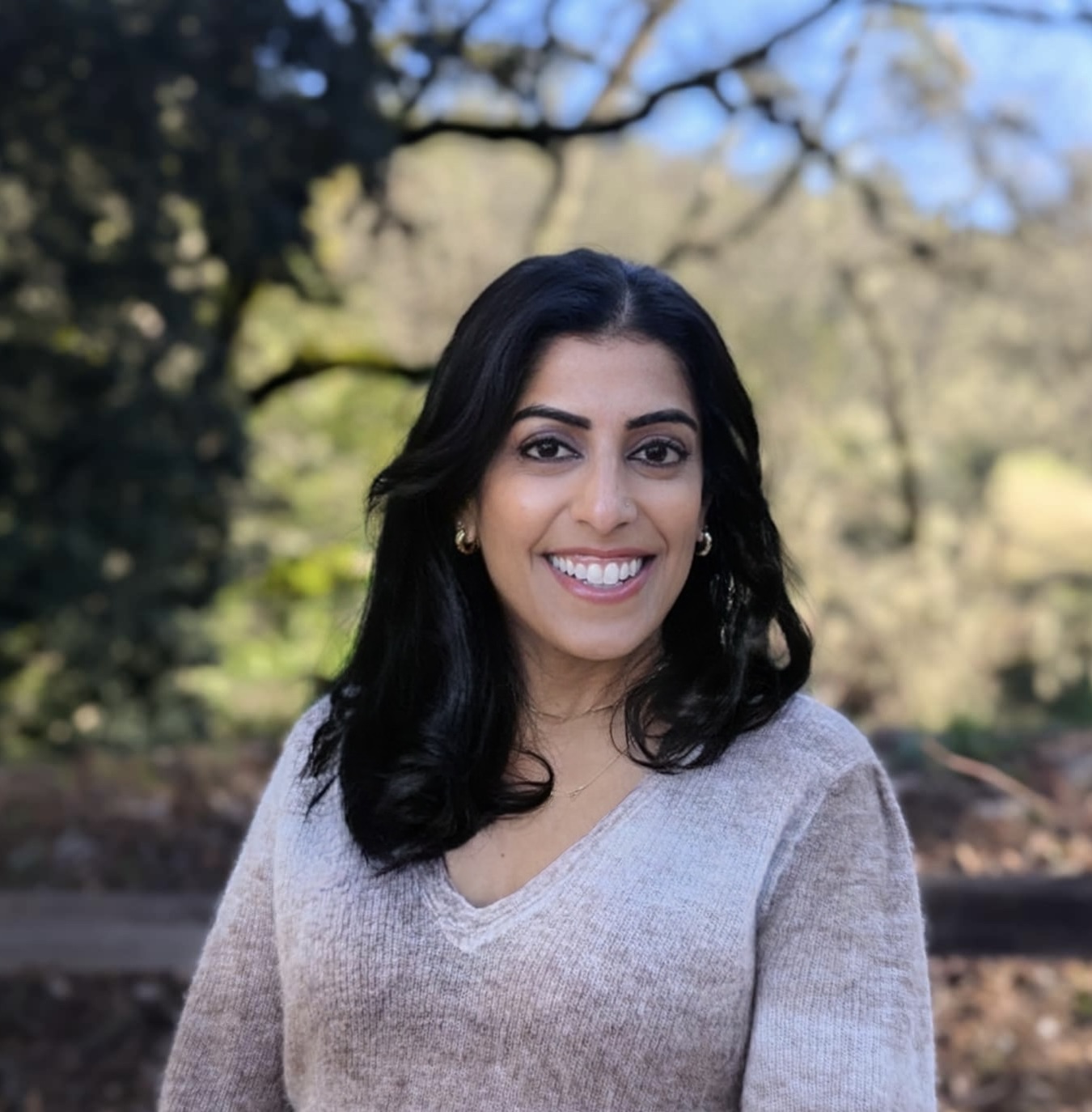 A headshot photo of Anjuli Arora-Dow smiling, wearing a dark blue shirt.
